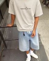 Remera oversize color beige de corte holgado, con estampa en la espalda que representa un esqueleto dentro de un ataúd con rayos oscuros y texto descriptivo.