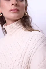 Sweater de punto color bordó con cuello alto y diseño de trenzas en el frente y las mangas. Presenta un corte holgado y largo, con puños y ruedo acanalados.