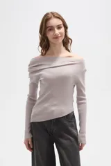 Sweater de punto acanalado color gris claro, con diseño de hombros descubiertos y cuello asimétrico drapeado. Presenta mangas largas y un corte ajustado al cuerpo.