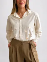 Camisa de algodón color beige con cuello clásico redondeado, manga larga y botonera oculta. Presenta apliques circulares en relieve distribuidos en el frente.