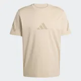 Remera de algodón color beige con cuello redondo y mangas cortas. Presenta el logo de Adidas estampado en el centro del pecho en un tono más oscuro y detalles gráficos en las mangas.