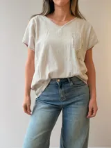 Remera de lino y algodón color beige con escote en V, mangas cortas y calce relajado. Presenta un bolsillo frontal decorado con apliques de strass, encaje y tachas, además de sutiles estampas con escritura manuscrita y detalles desflecados.