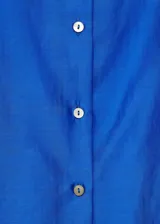 Camisa de corte recto y tejido satinado color azul eléctrico, con cuello camisero, manga larga con puños abotonados y cierre frontal de botones.