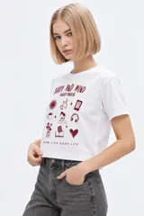 Remera de manga corta de algodón, color blanco, con cuello redondo y estampado frontal estilo collage con gráficos y texto en tono bordó.