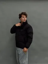 Campera puffer negra con diseño de paneles, cierre frontal completo y cuello alto. Presenta una textura diferenciada en la parte superior y bolsillos laterales.