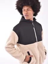 Campera con cierre frontal, capucha y diseño de bloques de color. La parte principal del cuerpo y las mangas son de tejido de borrego (teddy) color beige claro, mientras que los hombros, la capucha y los bordes son de tela negra lisa.