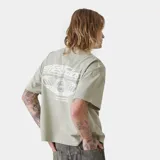 Camiseta beige de corte "boxy fit" con estampado blanco en la espalda que incluye el texto "emestudios" y un diseño gráfico con estrellas y texto adicional.