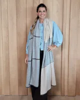 Bufandón de lana lambswool, diseñado para ser utilizado como ruana, con diseño de bloques de color en tonos gris y beige, y detalles de líneas horizontales oscuras.
