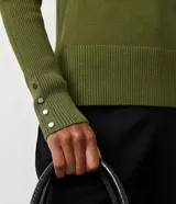 Suéter de punto color rosado, con cuello barco, mangas largas y puños con botones decorativos. El dobladillo también es acanalado.