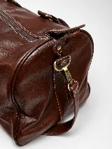Bolso de viaje color marrón, confeccionado en cuero vacuno, con doble asa de mano y correa ajustable y desmontable. Cuenta con herrajes metálicos y costuras reforzadas.