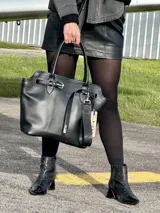 Cartera tipo tote de cuero genuino en color negro, con diseño estructurado, doble asa de mano y detalle de correa decorativa con hebilla y etiqueta colgante.
