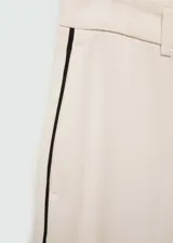 Pantalon de corte wideleg en color beige, confeccionado en tejido fluido. Presenta diseño de rayas laterales en contraste, trabillas para cinturón, dos bolsillos laterales y cierre oculto de botón, gancho y cremallera.