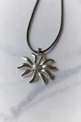 Collar con dije de acero quirúrgico en forma de flor tipo margarita, montado sobre un tiento de cuero negro.