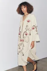 Vestido midi color crudo con bordados florales multicolores, escote en pico con lazos y mangas tres cuartos. Confeccionado en mezcla de algodón y lino.