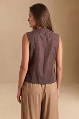 Blusa de algodón sin mangas en color blanco off-white, con cuello alto con volados y cierre frontal de cordones ajustables con lazos. Presenta detalles de encaje y bordados sutiles en la parte delantera.