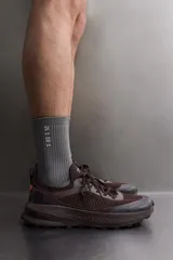 Zapatilla deportiva de correr para trail running, color marrón oscuro. Presenta una parte superior de tejido de punto transpirable, puntera y talón reforzados con material Shield Protect Max. Cuenta con ajuste de cordones, tirador trasero, plantilla OrthoLite® extraíble, entresuela Spume Foam V2 y suela de goma.