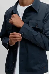 Cazadora técnica de corte recto y estilo utilitario, color azul marino. Presenta cuello clásico, cierre frontal con botones y dos bolsillos con solapa y botón en el pecho.