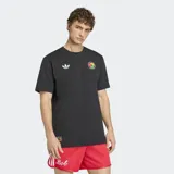 Remera negra de algodón con cuello redondo y mangas cortas. Presenta el logo del Trifolio de Adidas en blanco en el pecho derecho y un parche circular con manos entrelazadas en colores rasta en el pecho izquierdo. Incluye un pequeño parche rectangular en la parte inferior derecha.