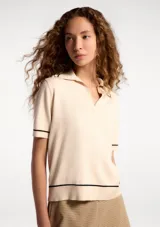 Polo de manga corta en tejido de punto color beige, con cuello tipo polo y detalles de líneas finas en color negro en el cuello, mangas y ruedo.