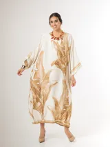Vestido maxi túnica de corte oversized, color beige y blanco con estampa de hojas de palmera en tonos camel, mangas murciélago y bolsillos laterales.