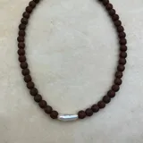 Collar artesanal compuesto por cuentas de piedra volcánica en diversos tonos y tamaños, con una perla natural de río como dije central y cierre metálico dorado.