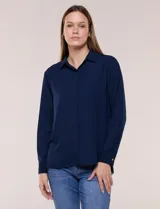 Camisa blanca de corte clásico y caída fluida, con cuello camisero tradicional, abotonadura frontal oculta y mangas largas con puños anchos.