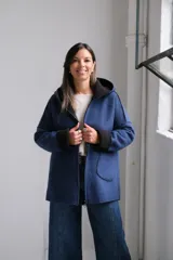 Tapado de paño azul con capucha, diseño de corte holgado y largo a la cadera. Presenta detalles en color negro en el interior, bordes y puños, con bolsillos frontales amplios y cierre frontal.
