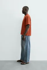 Camiseta de manga corta y cuello redondo, color terracota, con un pequeño bordado de una flor amarilla y la inscripción "Abstract Harmony" en el pecho.