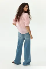 Blusa color rosado con cuello mao y botones ocultos en la parte delantera. Tiene canesú de doble capa con frunces adelante y atrás, mangas cortas abullonadas y puños con abertura y botón.