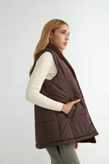 Chaleco acolchado color chocolate con interior y cuello de corderito sintético. Presenta cierre frontal con botones a presión y bolsillos laterales.