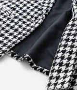 Blazer de sastrería confeccionado en tejido tweed con estampado pied de poule en blanco y negro. Presenta cuello con solapa, cierre frontal con un botón, mangas largas y bolsillos frontales con solapa.