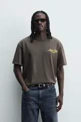 Camiseta de corte relajado con cuello redondo y manga corta. Presenta un efecto lavado y estampados a contraste en el frente y la espalda.