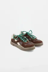 Championes urbanos de cuero en combinación de tonos marrones, con detalles en color crema y cordones verdes con motas blancas. Presentan una suela de goma color marrón y diseño de paneles superpuestos.