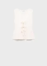 Top sin mangas de tejido de punto fino con textura acanalada. Presenta un diseño evasé, cuello escotado y cierre frontal mediante lazos decorativos.
