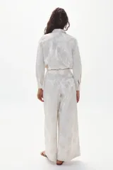 Pantalón culotte color marfil con estampado floral en brocato, de tiro alto con tablas, piernas anchas, bolsillos laterales y cierre frontal escondido.