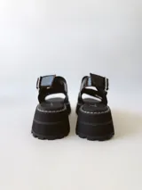 Sandalias negras de cuero con tiras cruzadas, plataforma track y hebilla lateral.