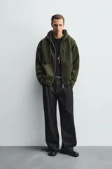 Sudadera de corte relajado confeccionada en tejido técnico con elasticidad y efecto neopreno. Presenta capucha ajustable con cordones, cierre frontal de cremallera de doble dirección, bolsillos tipo canguro y terminaciones en rib.