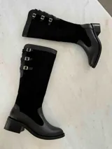 Bota alta de cuero negro con caña alta y taco cuadrado. Presenta tres correas con hebillas plateadas en la parte superior de la caña. Fabricada en Colombia.