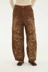 Pantalón de jean marrón de tiro alto y calce amplio, con bordados florales en contraste a lo largo de las piernas y bolsillos funcionales.