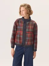 Campera tipo bomber de silueta relajada, confeccionada en una combinación de denim y tejido a cuadros en tonos marrones, azules y rojizos. Presenta cuello alto, cierre frontal y detalles de ribetes en color rojo vibrante en los bolsillos delanteros.