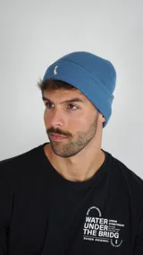 Gorro tipo beanie de tejido de punto acanalado en color azul, con diseño de doblez y logo bordado en la parte frontal.