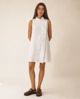 Vestido corto blanco sin mangas, confeccionado en lino, con cuello alto, cierre frontal cruzado con botones forrados y detalle de volado lateral.