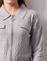 Cardigan de tejido jacquard color gris con diseño geométrico en relieve. Presenta cuello con solapa, cierre frontal completo y bolsillos decorativos en el pecho.