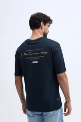 Remera oversize verde militar, confeccionada en 100% algodón, con cuello redondo y diseño relajado. Presenta un pequeño bordado frontal en tono naranja.