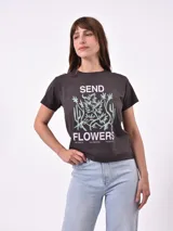 Remera de algodón color gris oscuro con cuello redondo y mangas cortas. Presenta un estampado frontal con la frase 'SEND FLOWERS' en letras rosadas y un diseño gráfico de plantas en color verde claro.