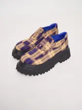 Mocasines con plataforma de goma negra, confeccionados en lona con estampa a cuadros en tonos violeta, amarillo y beige, y detalle de elásticos laterales ocultos.