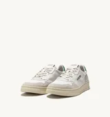 Championes de estilo vintage inspirados en los años 80, confeccionados en cuero blanco con paneles de gamuza gris en la puntera y el talón. Presentan perforaciones en la puntera para mayor ventilación, cordones planos de algodón y un detalle en color verde en el talón. La suela es de goma en tono crema con el logo de la marca.