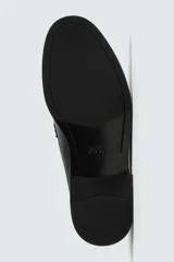 Mocasín de vestir color marrón oscuro, con parte superior lisa, detalle de antifaz con borlas en el empeine y horma redonda. Suela de goma a tono.