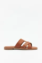 Sandalias bajas abiertas de símil cuero marrón, con capellada de tiras asimétricas cruzadas y detalle de tachas metálicas doradas.