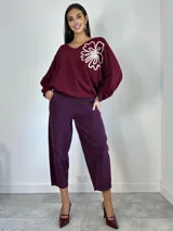 Sweater de punto oversized color verde, con escote en V y manga larga. Presenta un aplique bordado en forma de flor en el hombro izquierdo.